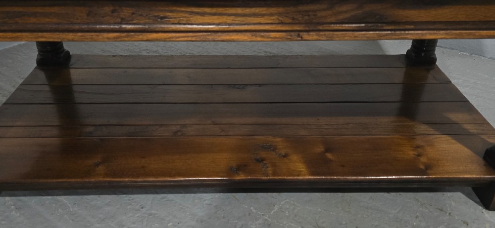 A rectangular dark oak coffee table featuring a plank top, turned legs, and a lower slatted shelf. View VII