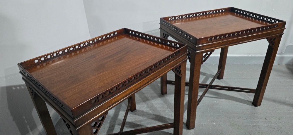 A matching pair of dark mahogany Chippendale-style lamp tables featuring pierced fretwork galleries, corner brackets, and X-frame stretchers. View X