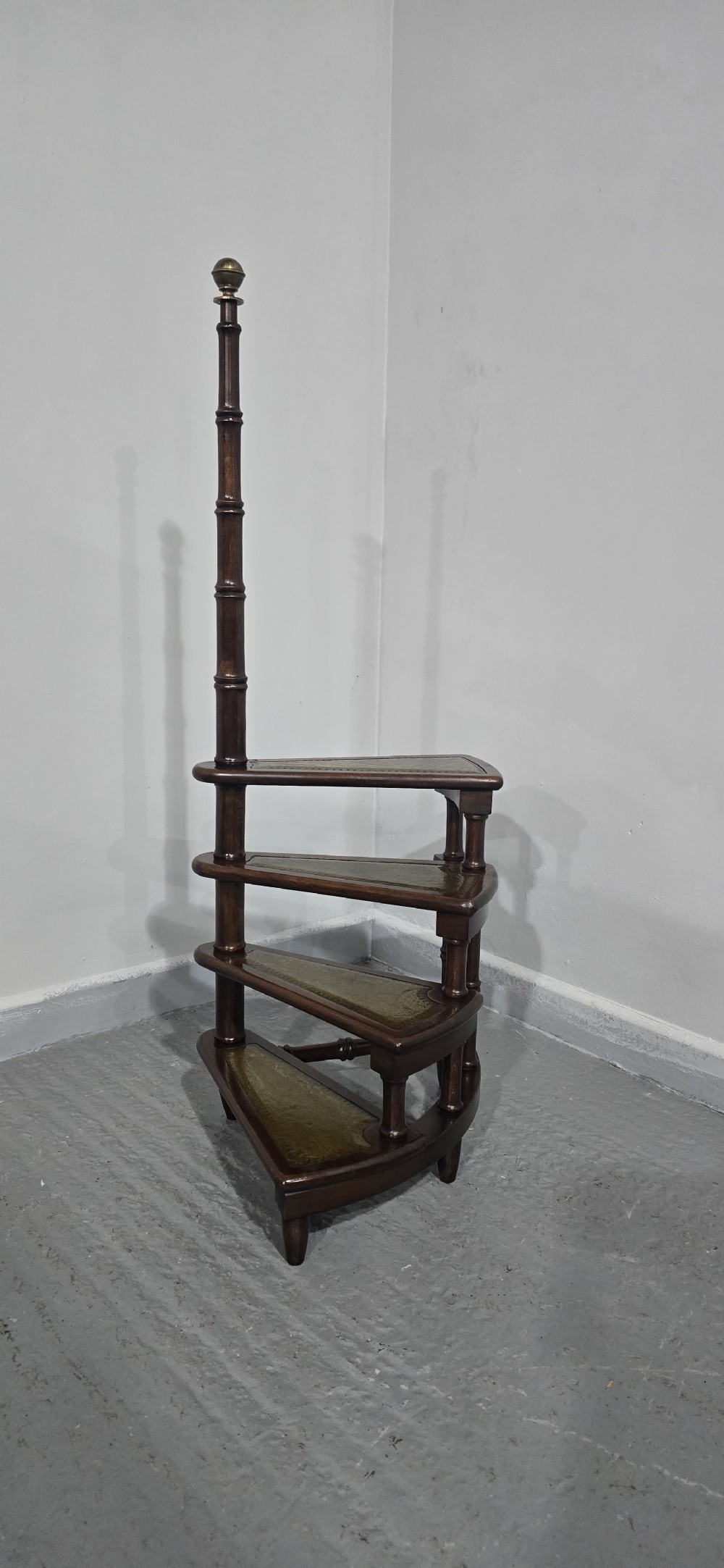 A set of four dark mahogany spiral library steps with green leather inset treads and a tall pole topped with a brass finial. View III