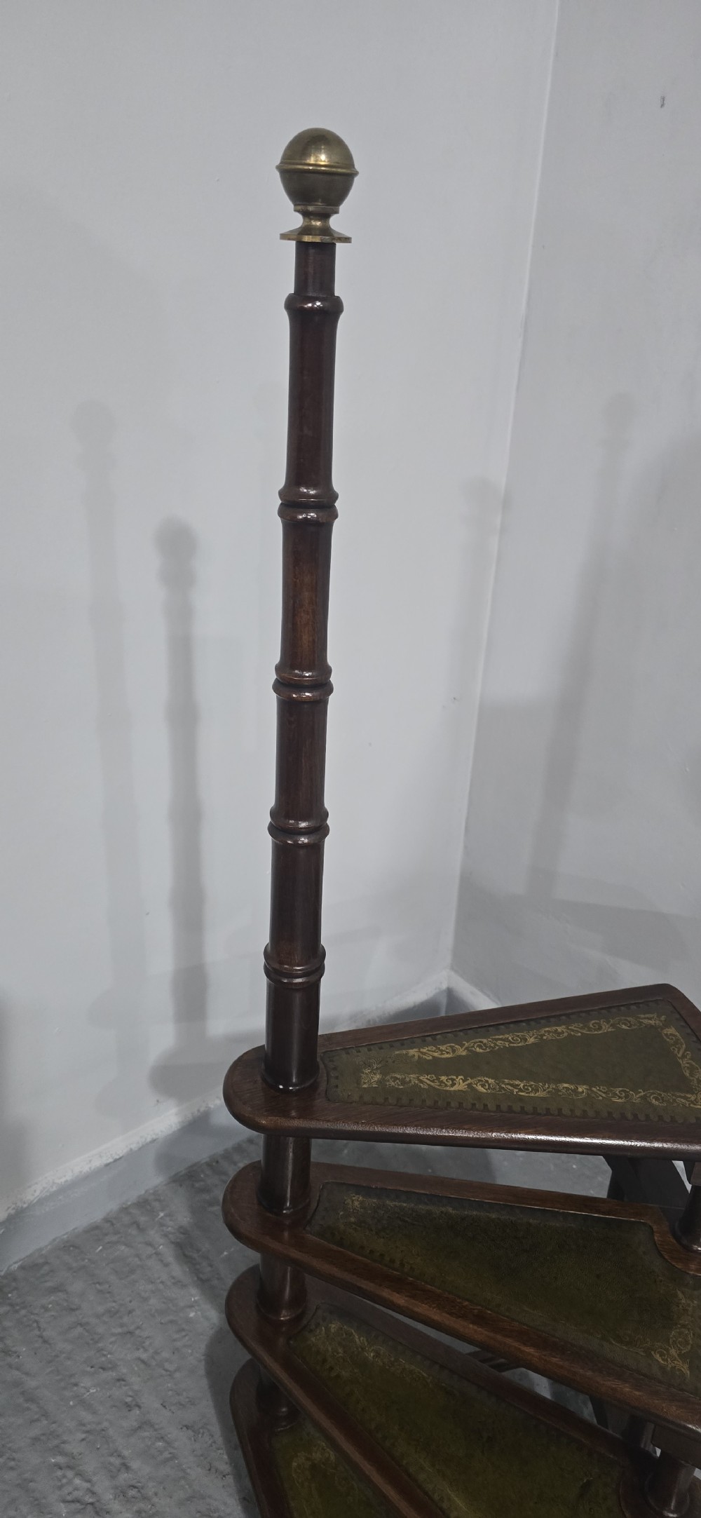 A set of four dark mahogany spiral library steps with green leather inset treads and a tall pole topped with a brass finial. View V