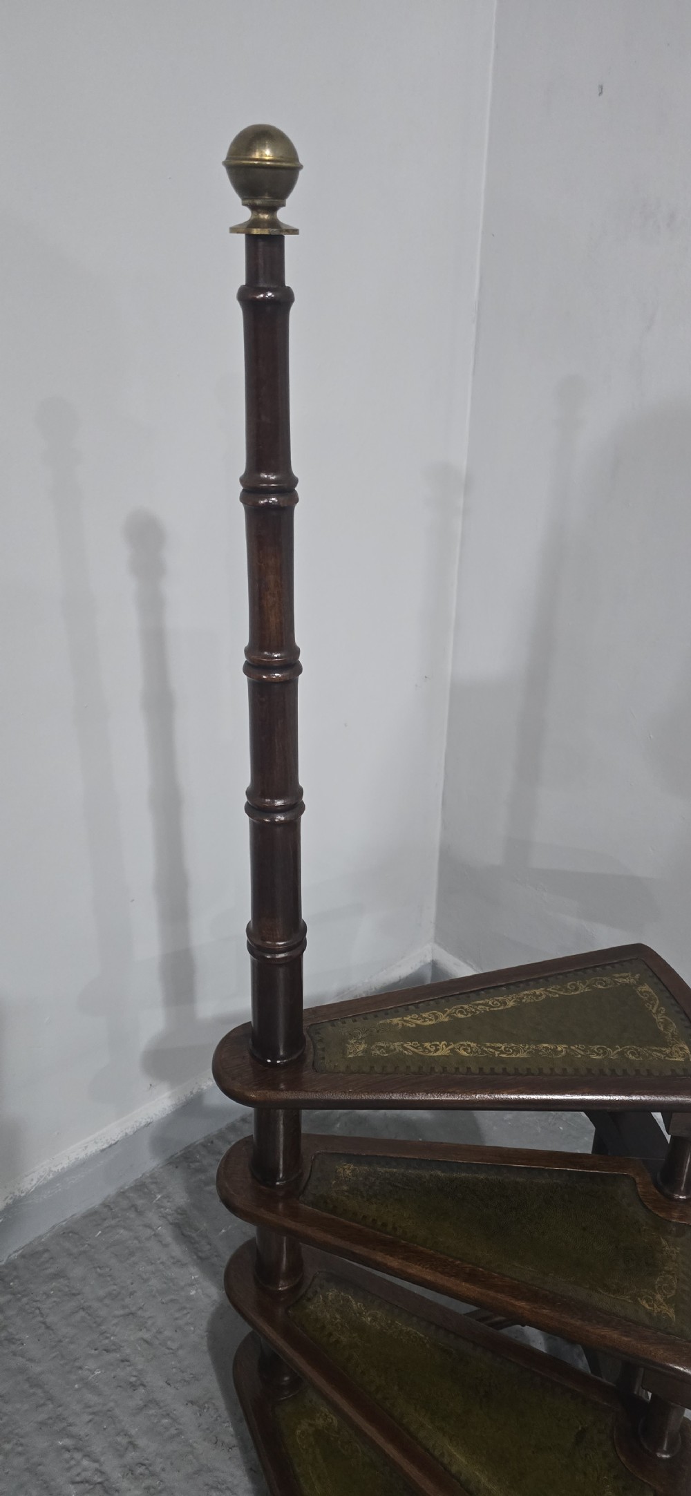 A set of four dark mahogany spiral library steps with green leather inset treads and a tall pole topped with a brass finial. View VI