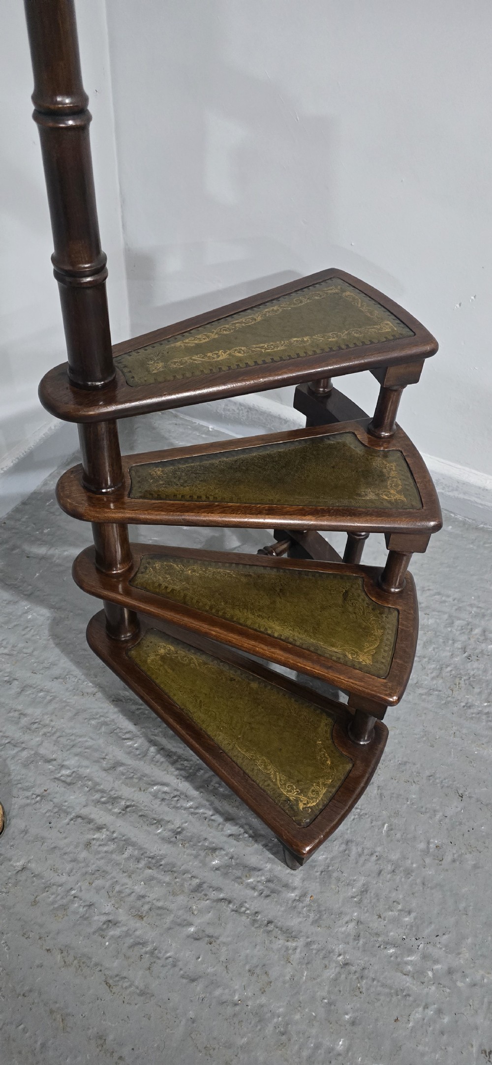 A set of four dark mahogany spiral library steps with green leather inset treads and a tall pole topped with a brass finial. View X