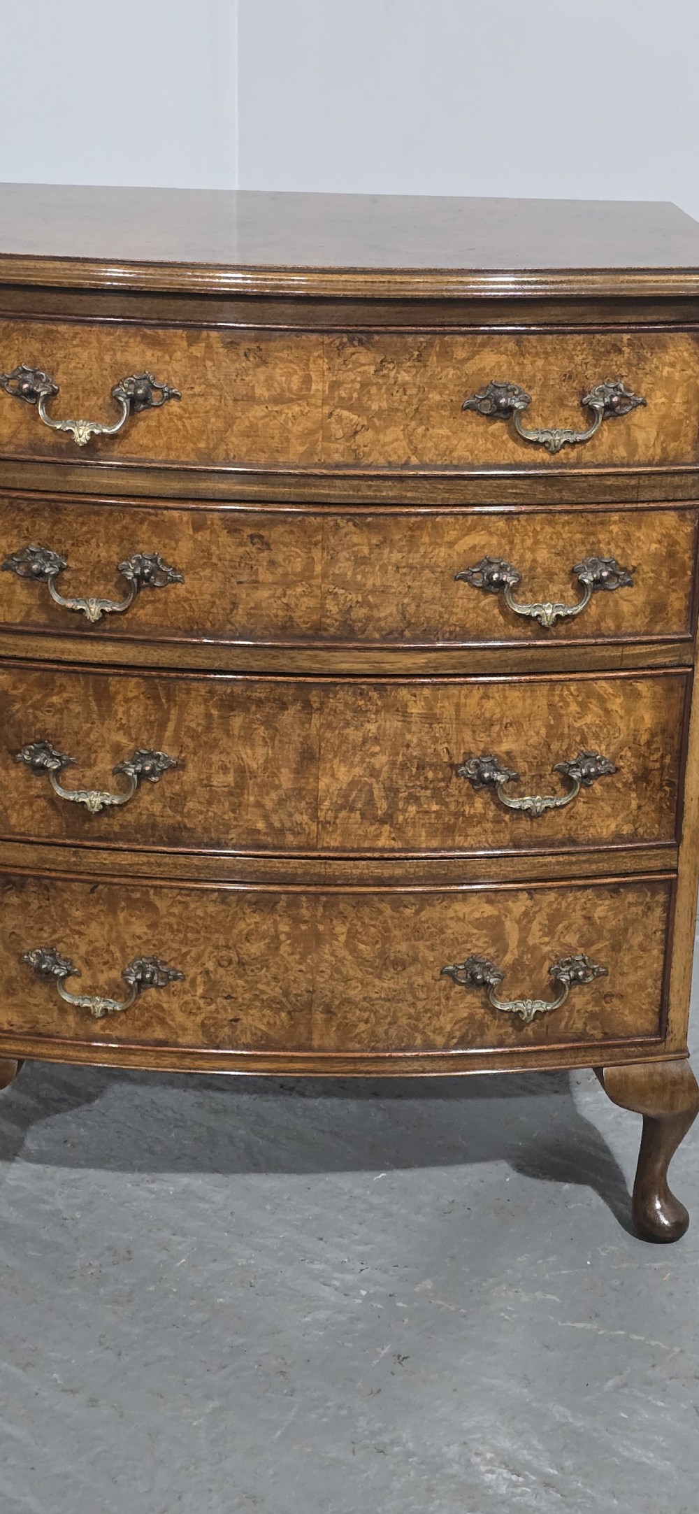 A Queen Anne style burr walnut chest of four graduated drawers featuring a gently curved bow front, brass handles, and cabriole legs. View IV