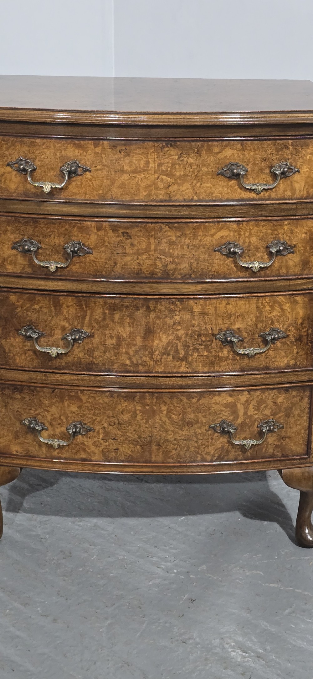 A Queen Anne style burr walnut chest of four graduated drawers featuring a gently curved bow front, brass handles, and cabriole legs. View V