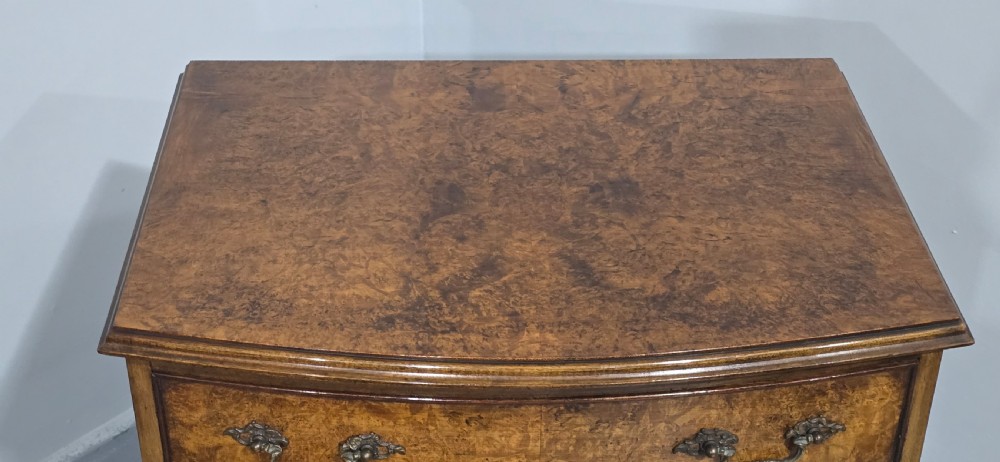 A Queen Anne style burr walnut chest of four graduated drawers featuring a gently curved bow front, brass handles, and cabriole legs. View VIII