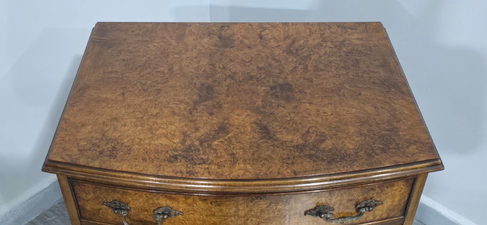A Queen Anne style burr walnut chest of four graduated drawers featuring a gently curved bow front, brass handles, and cabriole legs. View X