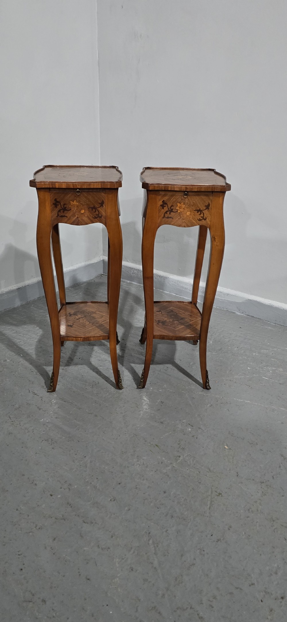 A pair of slender warm brown French marquetry tables featuring floral inlays, cabriole legs, lower shelves, and extended side drawers. View XII