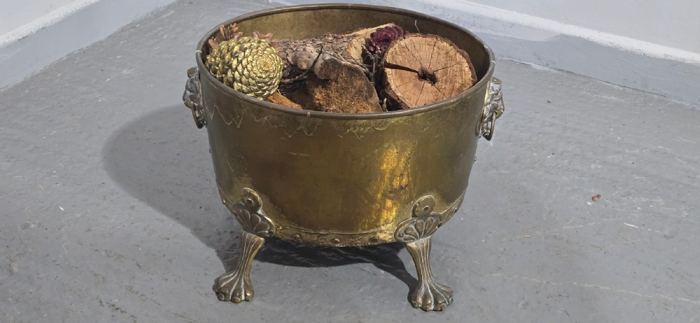 A circular antique brass log bin featuring cast lion mask handles and shell-crested claw feet. View III