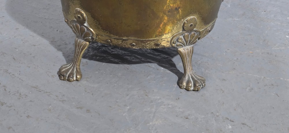 A circular antique brass log bin featuring cast lion mask handles and shell-crested claw feet. View IV