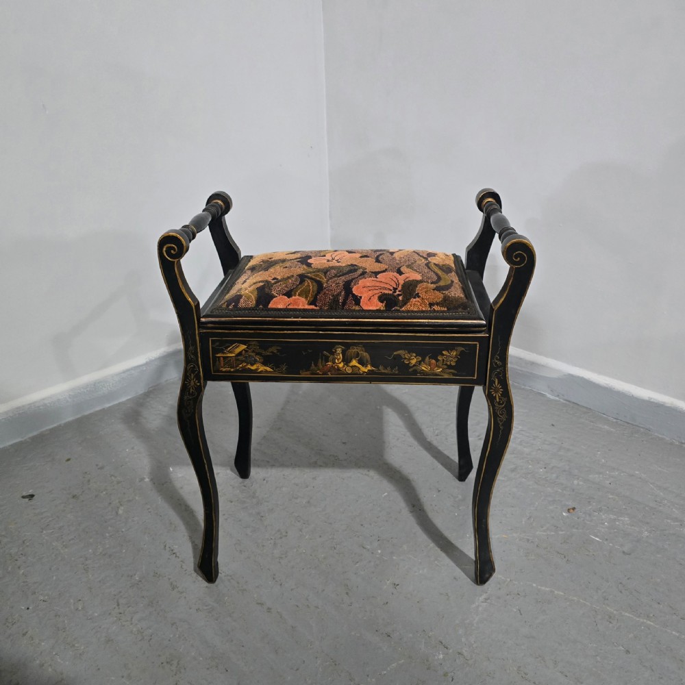 A black lacquered piano stool with hand-painted gold Chinoiserie designs, turned side handles, curved legs, and a floral tapestry seat. View II