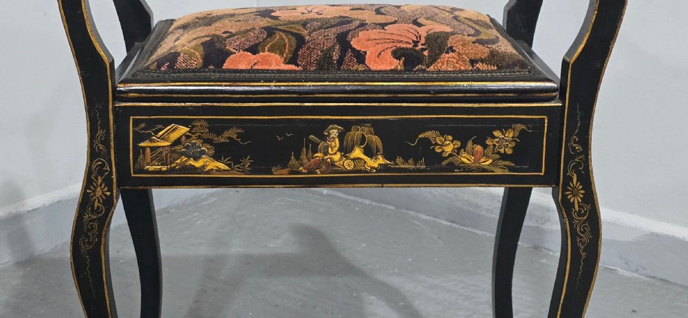 A black lacquered piano stool with hand-painted gold Chinoiserie designs, turned side handles, curved legs, and a floral tapestry seat. View III