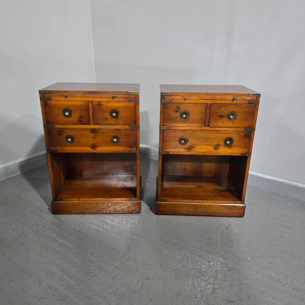 A pair of warm brown yew wood campaign style bedside tables featuring brass corner mounts, flush brass pull handles, drawers, and lower open shelves. View II