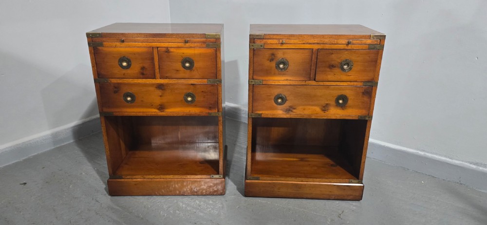 A pair of warm brown yew wood campaign style bedside tables featuring brass corner mounts, flush brass pull handles, drawers, and lower open shelves. View III