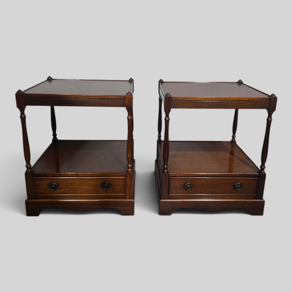 A pair of dark mahogany two-tier lamp tables with turned corner supports and single base drawers featuring brass ring handles.