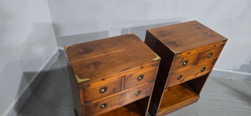 A pair of warm brown yew wood campaign style bedside tables featuring brass corner mounts, flush brass pull handles, drawers, and lower open shelves. View VIII