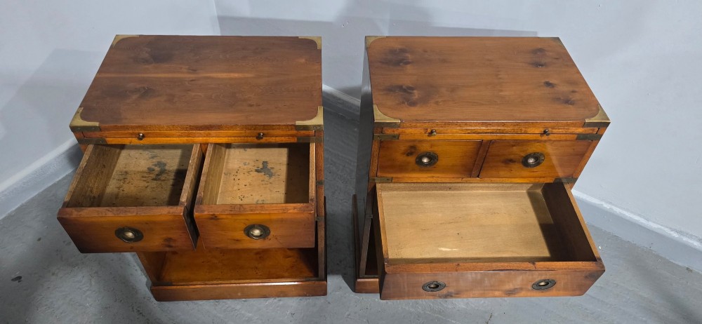 A pair of warm brown yew wood campaign style bedside tables featuring brass corner mounts, flush brass pull handles, drawers, and lower open shelves. View IX