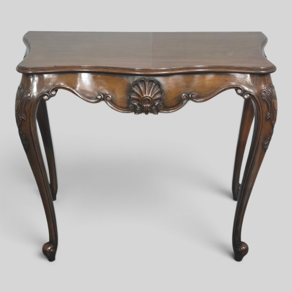 A dark mahogany console table featuring a shaped serpentine top, a central shell carving on the apron, and four cabriole legs.