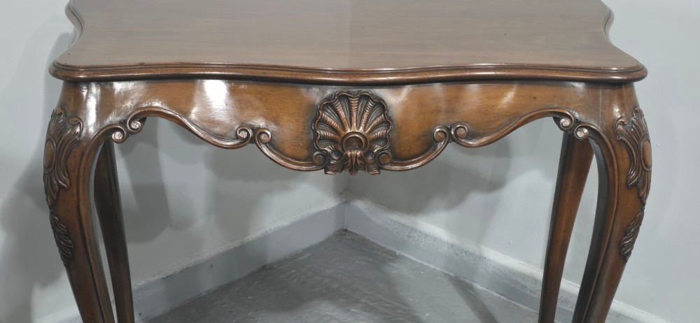 A dark mahogany console table featuring a shaped serpentine top, a central shell carving on the apron, and four cabriole legs. View IV