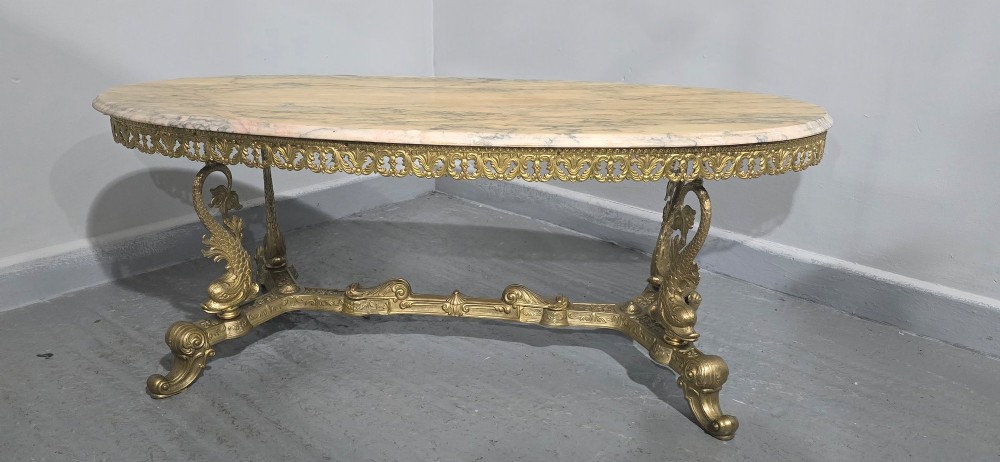 An oval gilt brass coffee table with an ornate pierced gallery apron, scrolled mythical legs, a central stretcher, and a polished veined pink marble top. View III
