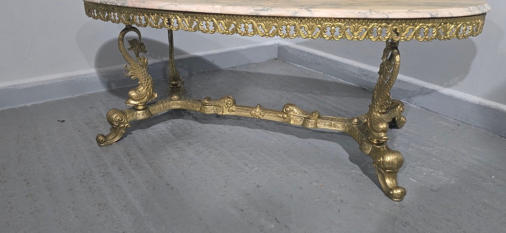 An oval gilt brass coffee table with an ornate pierced gallery apron, scrolled mythical legs, a central stretcher, and a polished veined pink marble top. View IV