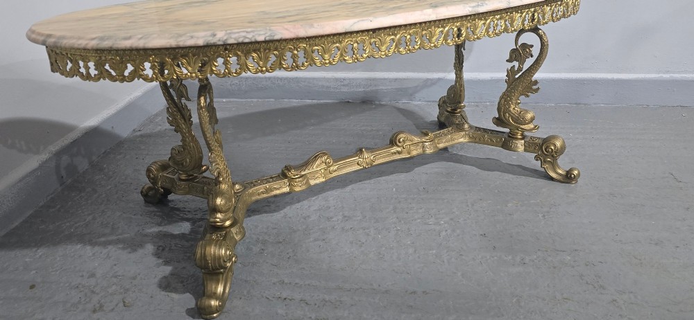 An oval gilt brass coffee table with an ornate pierced gallery apron, scrolled mythical legs, a central stretcher, and a polished veined pink marble top. View VIII