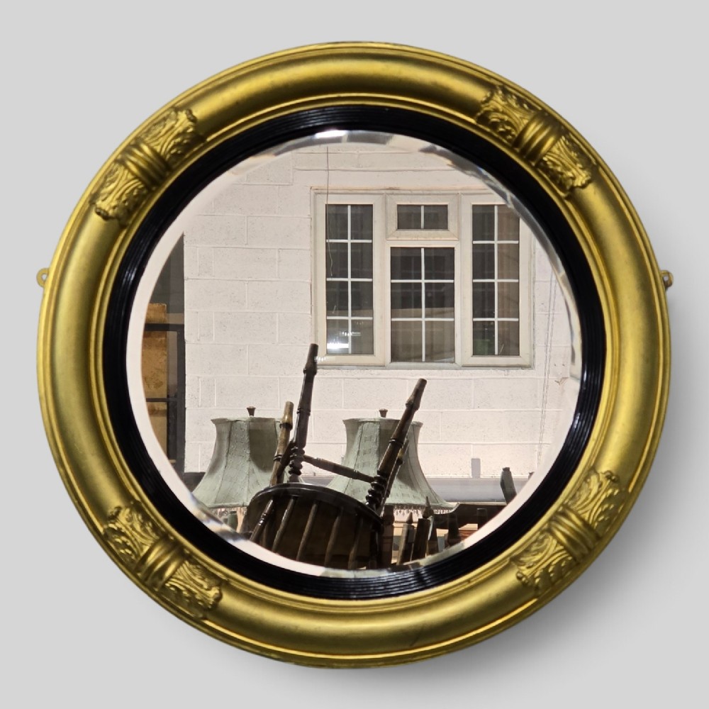 A circular Regency style giltwood mirror featuring a black inner reeded slip and classical acanthus leaf decorative accents on the moulded frame.
