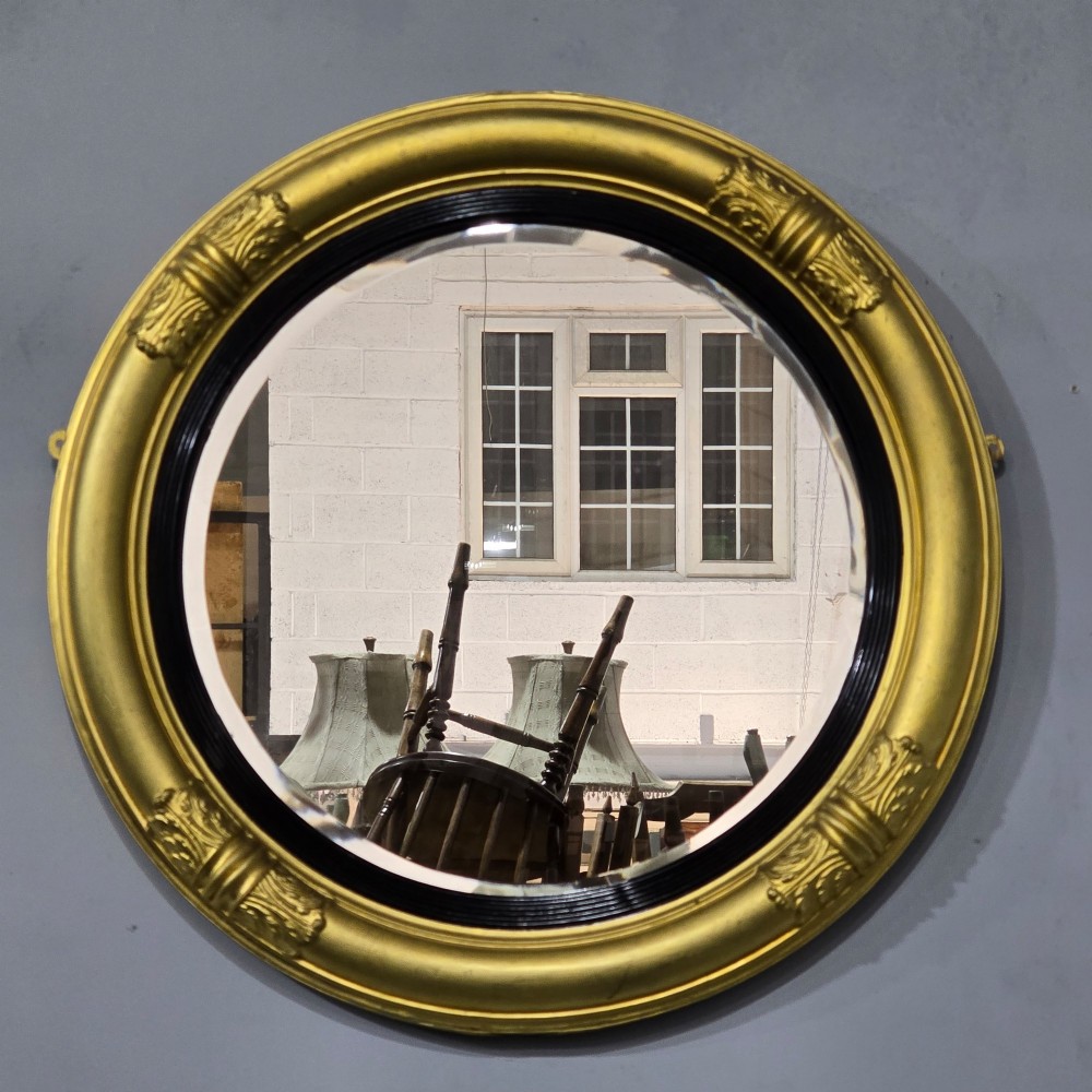 A circular Regency style giltwood mirror featuring a black inner reeded slip and classical acanthus leaf decorative accents on the moulded frame. View VIII