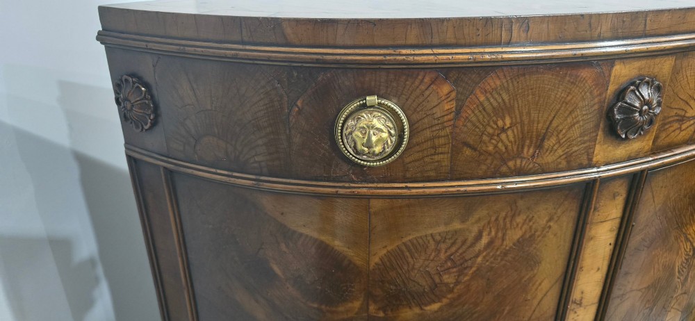 A semi-circular burr yew wood side cabinet featuring brass mounts along the frieze and central double doors. View IV