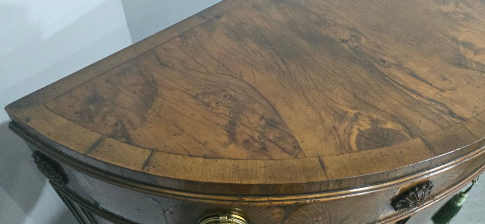 A semi-circular burr yew wood side cabinet featuring brass mounts along the frieze and central double doors. View IX
