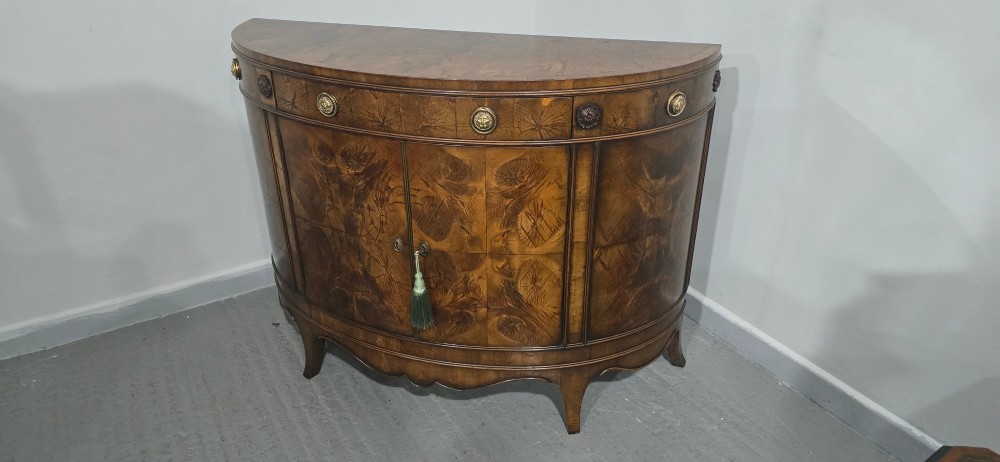 A semi-circular burr yew wood side cabinet featuring brass mounts along the frieze and central double doors. View X