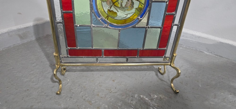 A brass fire screen featuring a leaded stained glass panel with a central hand-painted bird roundel set on splayed brass feet. View III