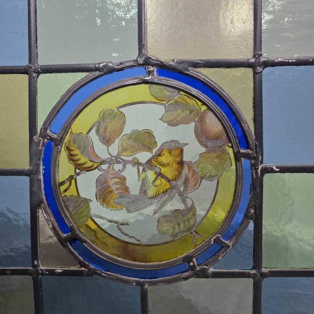 A brass fire screen featuring a leaded stained glass panel with a central hand-painted bird roundel set on splayed brass feet. View VI