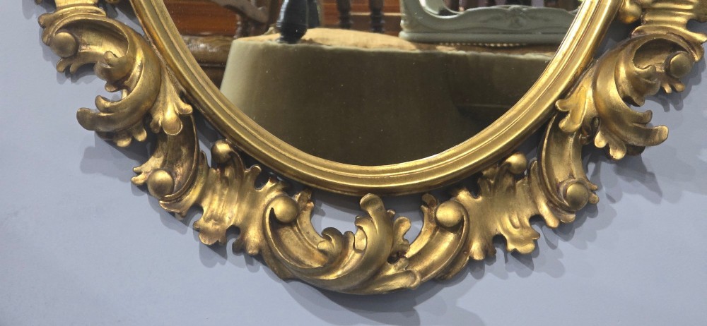 An oval wall mirror enclosed in a deeply carved gold giltwood frame featuring ornate acanthus leaf and scrolling foliage details. View VIII