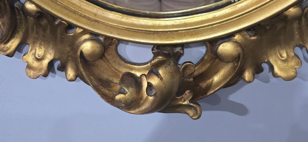 An oval wall mirror enclosed in a deeply carved gold giltwood frame featuring ornate acanthus leaf and scrolling foliage details. View XI