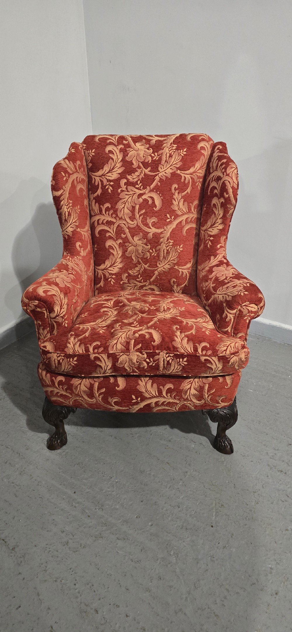 A high-backed wing armchair upholstered in red floral damask fabric with carved mahogany cabriole front legs featuring claw and ball feet. View II
