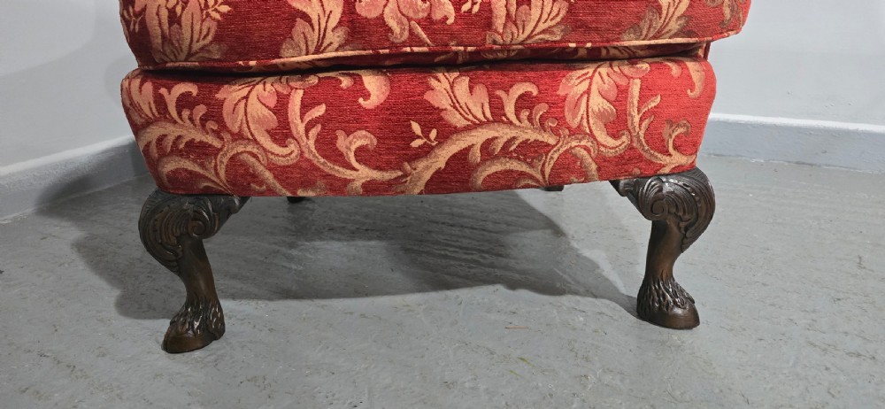 A high-backed wing armchair upholstered in red floral damask fabric with carved mahogany cabriole front legs featuring claw and ball feet. View III