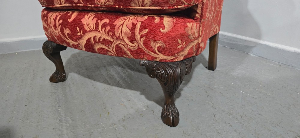 A high-backed wing armchair upholstered in red floral damask fabric with carved mahogany cabriole front legs featuring claw and ball feet. View V