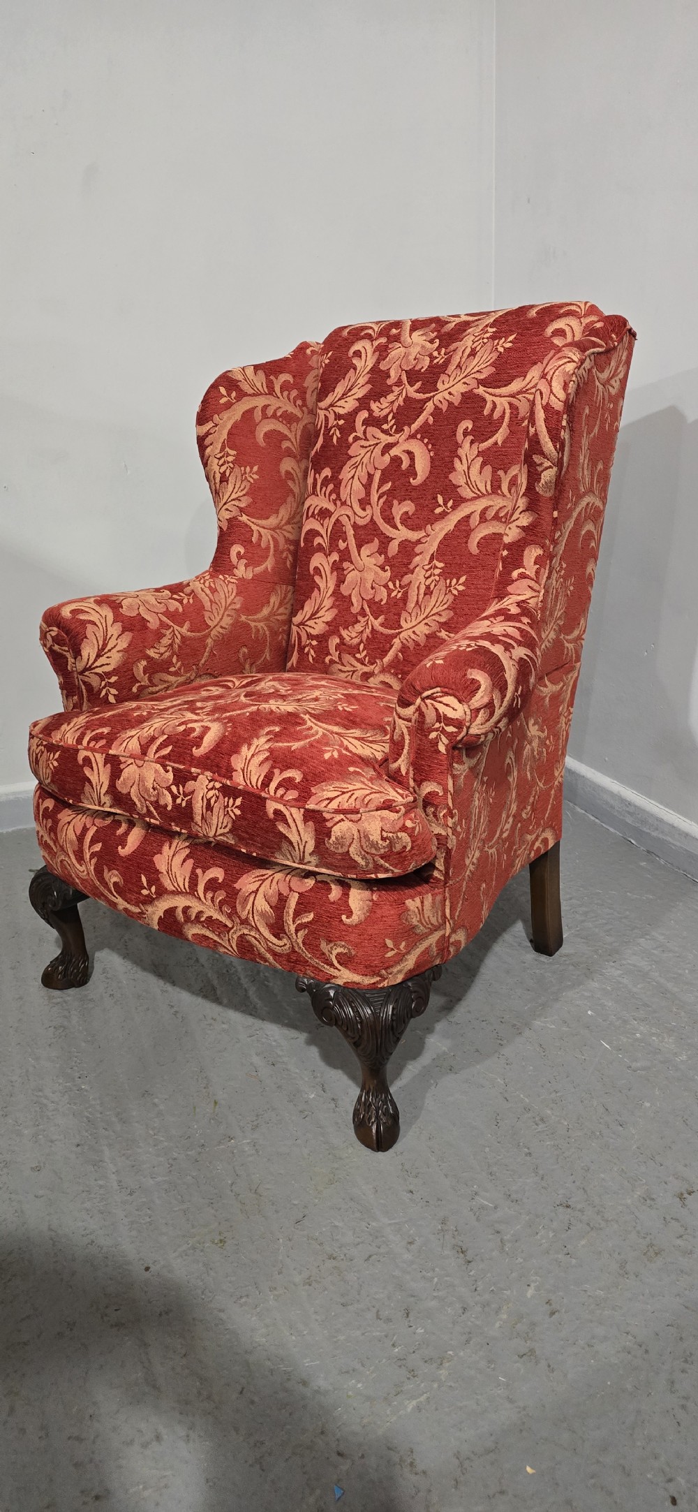 A high-backed wing armchair upholstered in red floral damask fabric with carved mahogany cabriole front legs featuring claw and ball feet. View VI