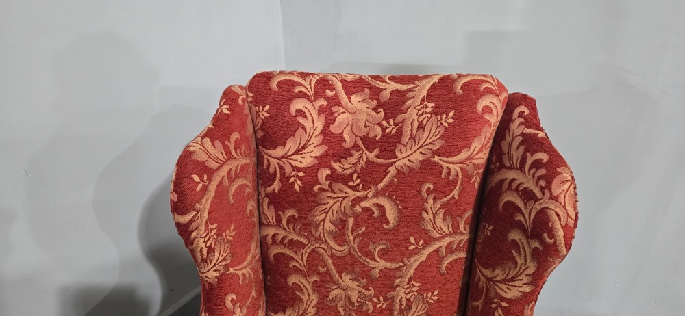 A high-backed wing armchair upholstered in red floral damask fabric with carved mahogany cabriole front legs featuring claw and ball feet. View VII