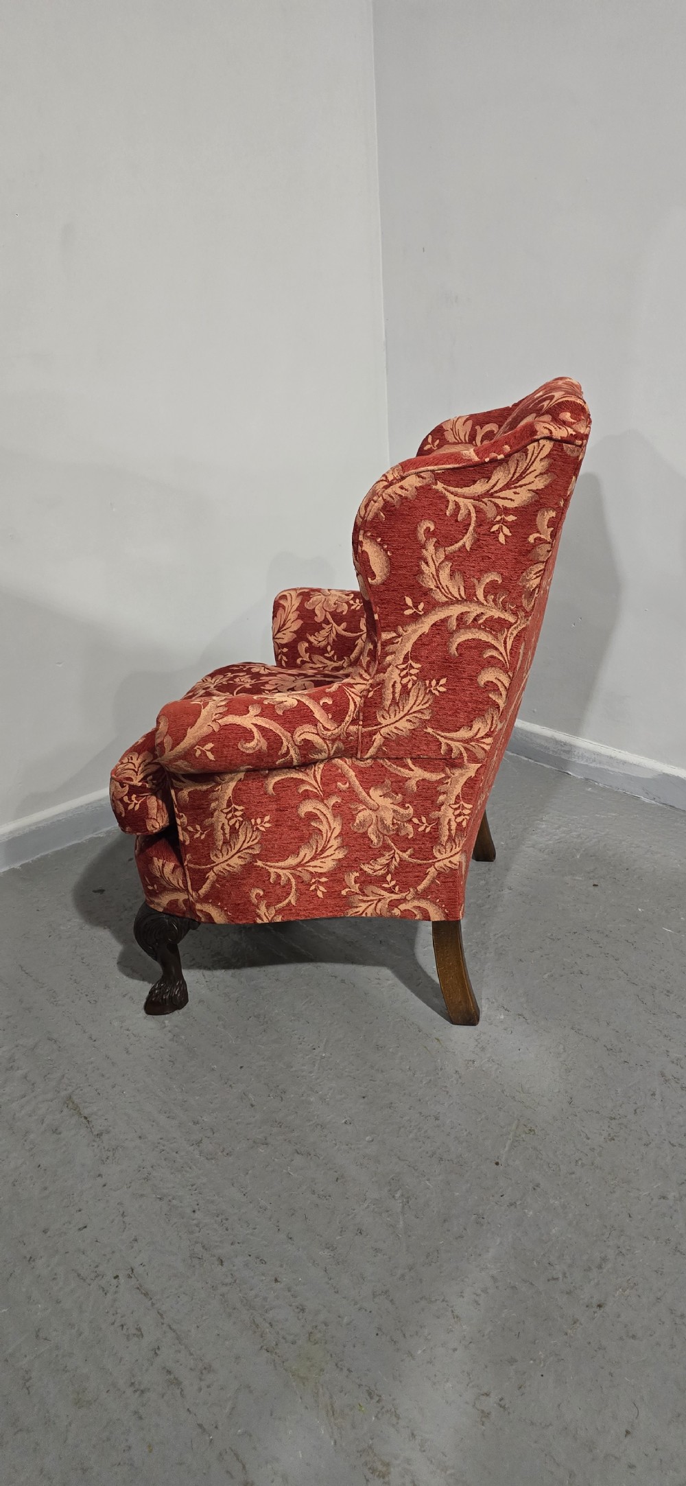 A high-backed wing armchair upholstered in red floral damask fabric with carved mahogany cabriole front legs featuring claw and ball feet. View IX