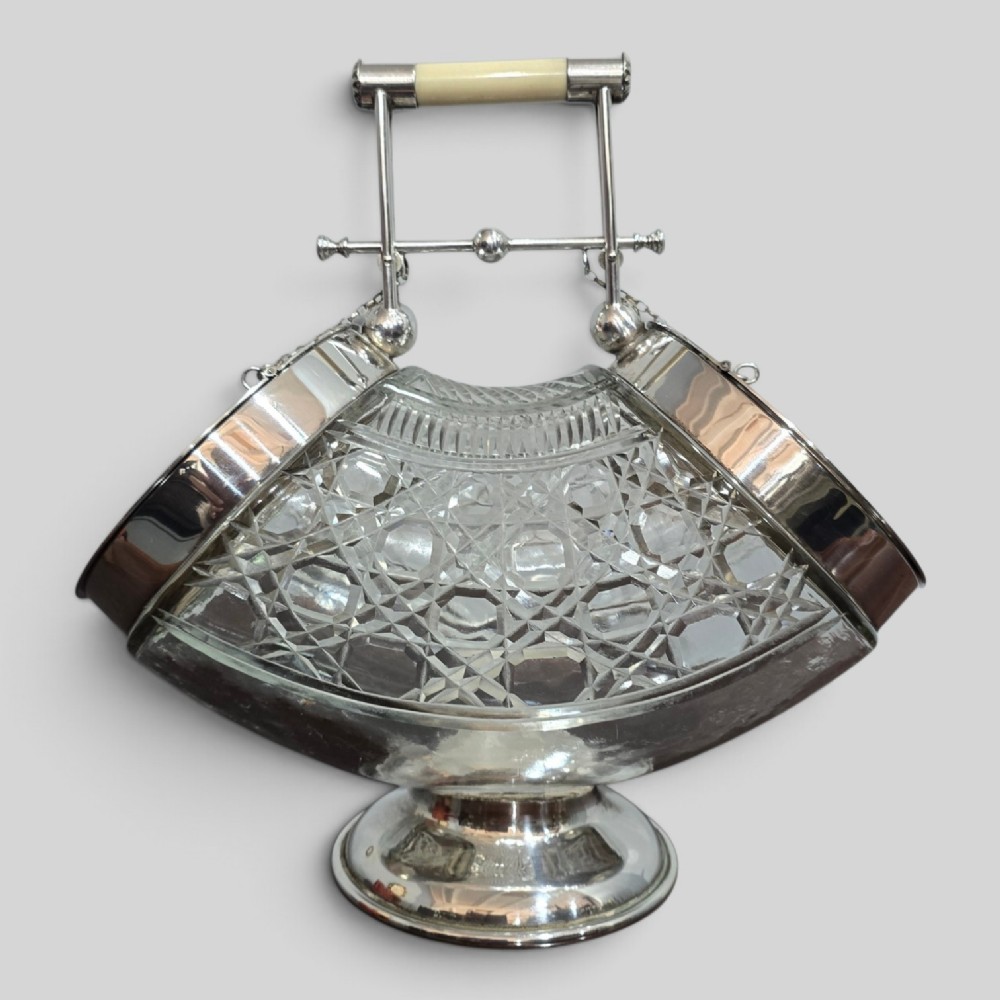 An Edwardian cut glass biscuit barrel featuring a hobnail geometric pattern, silver-plated frame, overhead handle, and pedestal base.