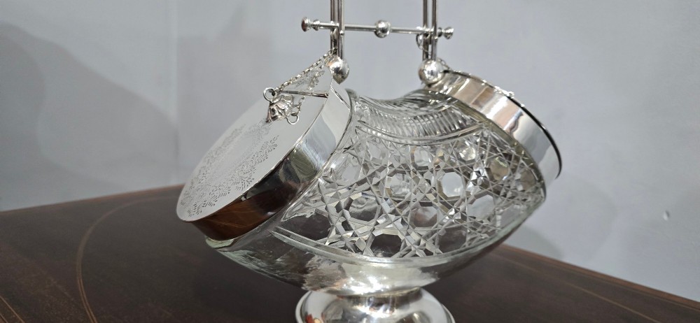 An Edwardian cut glass biscuit barrel featuring a hobnail geometric pattern, silver-plated frame, overhead handle, and pedestal base. View III