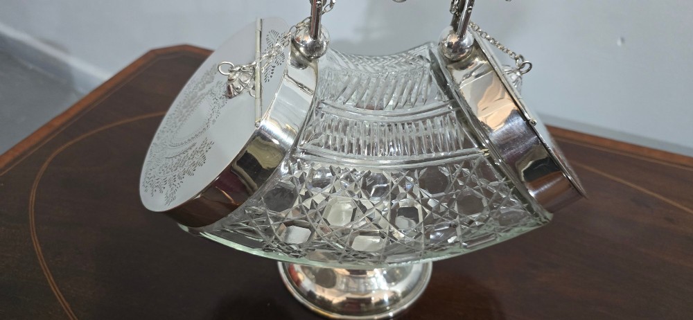 An Edwardian cut glass biscuit barrel featuring a hobnail geometric pattern, silver-plated frame, overhead handle, and pedestal base. View VII