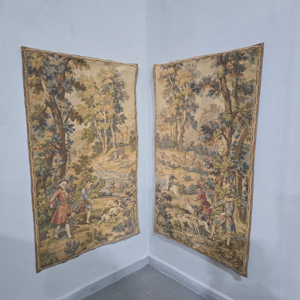 A pair of vertical woven French tapestries depicting men and hounds hunting within a dense green forest and natural landscape. View II