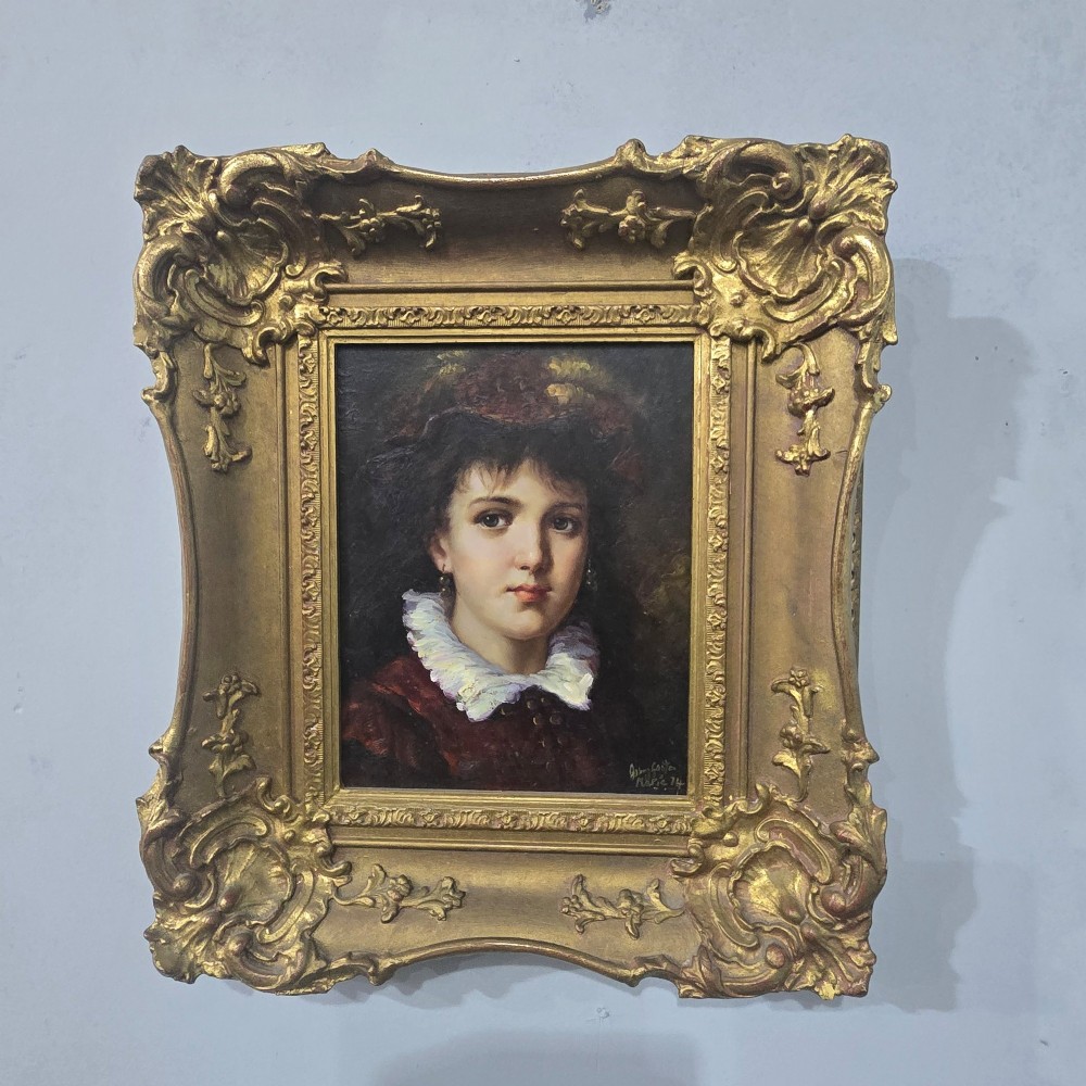 An oil painting on board depicting a young woman with dark hair and a ruffled white collar, displayed within a heavily carved gold Rococo style frame.