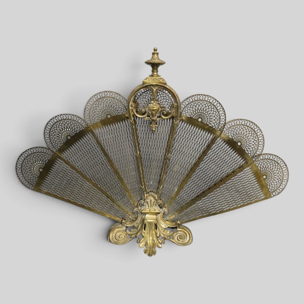 An ornate Victorian brass peacock fire screen featuring pierced filigree fan panels, a finial crest, and a cast scrollwork base.