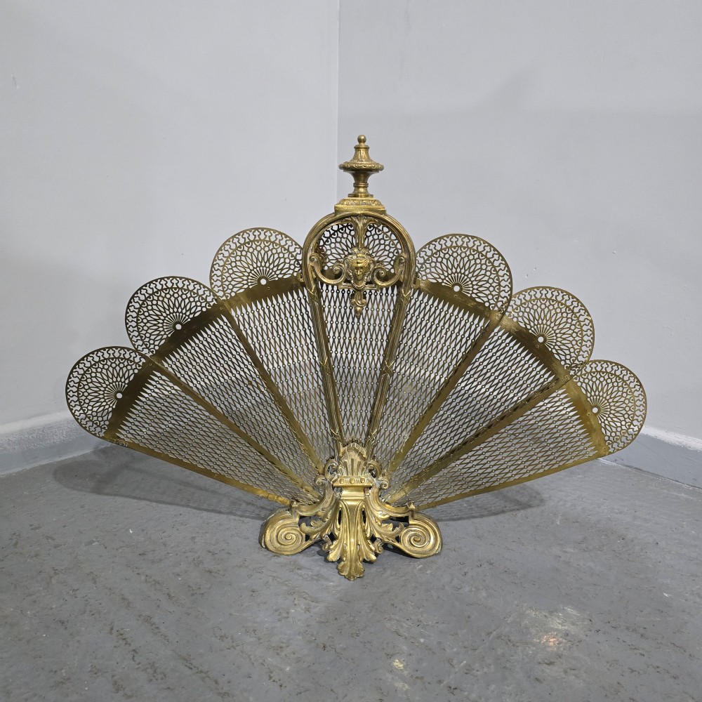 An ornate Victorian brass peacock fire screen featuring pierced filigree fan panels, a finial crest, and a cast scrollwork base. View IV