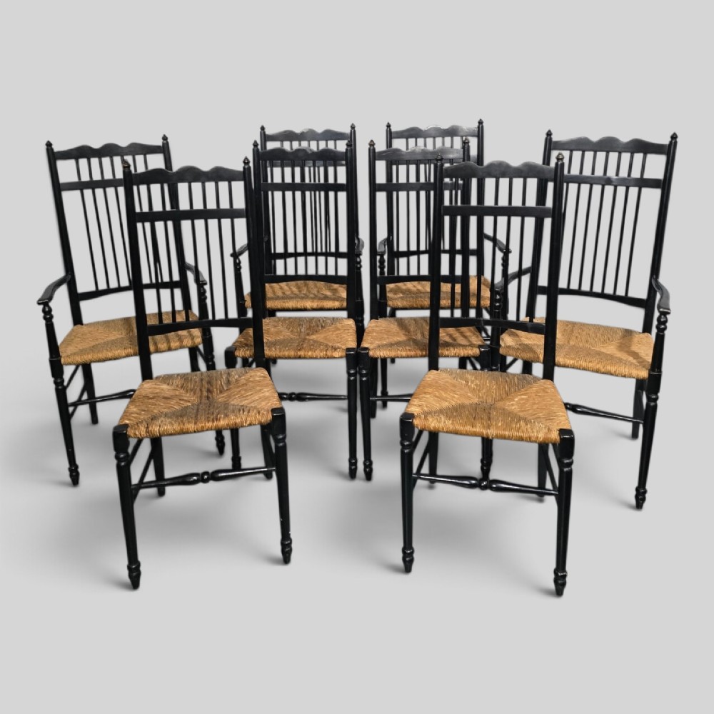 A set of eight Arts and Crafts ebonised wooden dining chairs featuring high spindle backs and hand-woven natural rush seats.