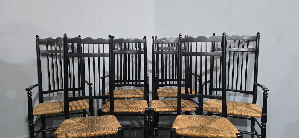 A set of eight Arts and Crafts ebonised wooden dining chairs featuring high spindle backs and hand-woven natural rush seats. View III