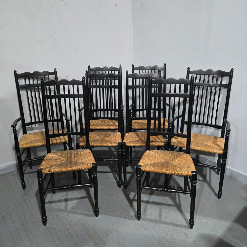 A set of eight Arts and Crafts ebonised wooden dining chairs featuring high spindle backs and hand-woven natural rush seats. View IX